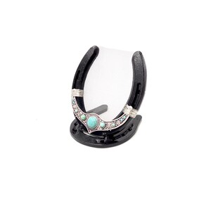 May include: Black horseshoe picture frame with a turquoise and silver design. The frame has a mesh backing and a small stand.