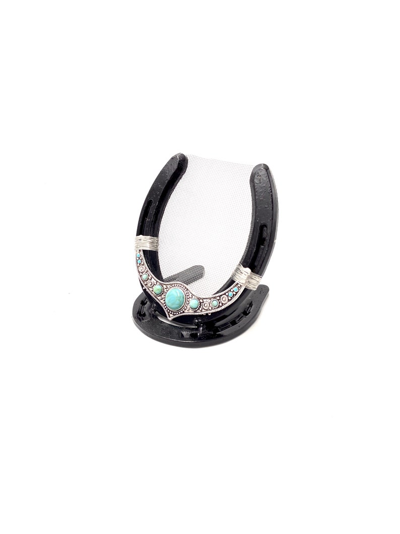 May include: Black horseshoe picture frame with a turquoise and silver design. The frame has a mesh backing and a small stand.