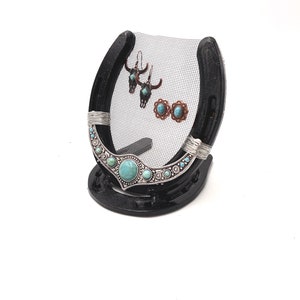 May include: Black horseshoe jewelry stand with a wire mesh backing. The stand has turquoise and silver accents and is holding a pair of earrings.