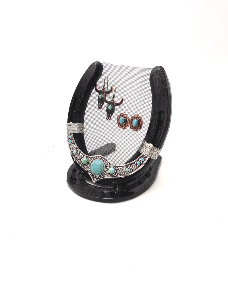 May include: Black horseshoe jewelry stand with a wire mesh backing. The stand has turquoise and silver accents and is holding a pair of earrings.