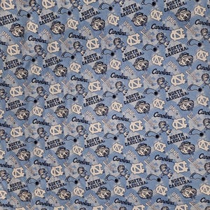 May include: Light blue fabric with a repeating pattern of UNC logos, Tar Heel mascots, and the words "North Carolina" and "Carolina" in white and navy blue. The fabric has a textured appearance.