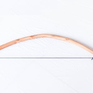 May include: A wooden bow with a string attached. The bow is made of light brown wood and has a natural finish. The string is black and is tied to the ends of the bow. The bow is on a white background.