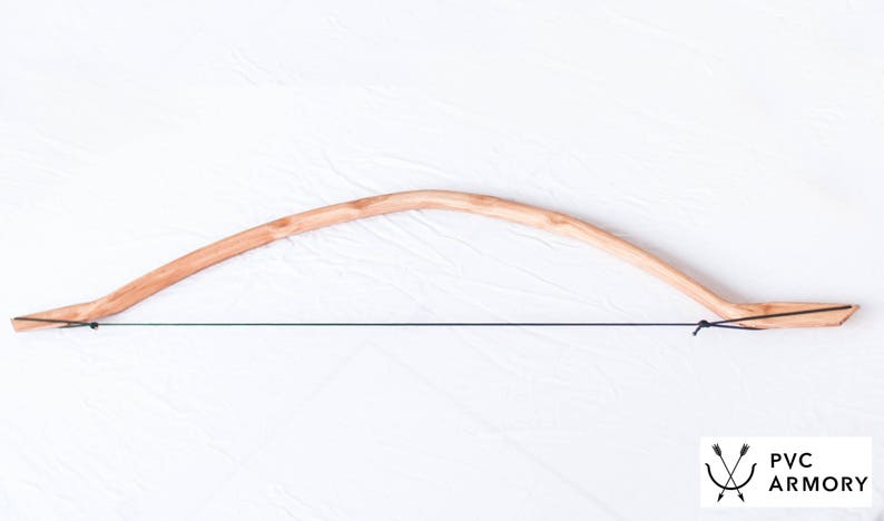 May include: A wooden bow with a string attached. The bow is made of light brown wood and has a natural finish. The string is black and is tied to the ends of the bow. The bow is on a white background.