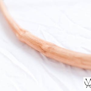 May include: A close-up of a wooden bow, showing the natural grain of the wood. The bow is curved and appears to be made of a single piece of wood.