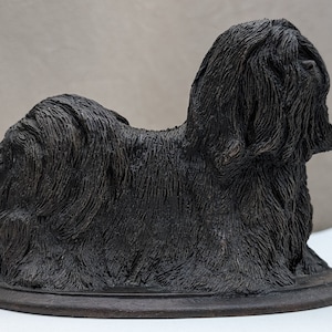 Puede incluir: Una figurita de cerámica negra de un perro Shih Tzu sentado sobre una base de madera.