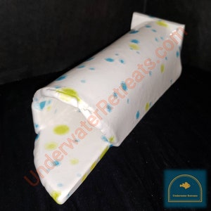 Peut inclure: Décoration d'aquarium en céramique blanche avec des pois bleus et jaunes. La structure cylindrique a une extrémité ouverte et un dessus rectangulaire. Le texte "UnderwaterRetreats.com" est visible sur le côté. Un logo avec un poisson est dans le coin inférieur droit.