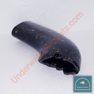 Puede incluir: Objeto curvo de color oscuro con acabado brillante. Presenta un patrón moteado de pequeños puntos claros y un borde rugoso y texturizado. El texto "UnderwaterRetreats.com" es visible en el fondo.