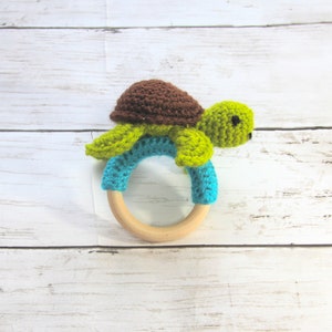 May include: A crocheted green and brown turtle attached to a wooden teething ring. The ring is blue and turquoise.