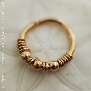 Pu&ograve; includere: Orecchino a cerchio in oro con un design a filo intrecciato e tre piccole perle dorate.