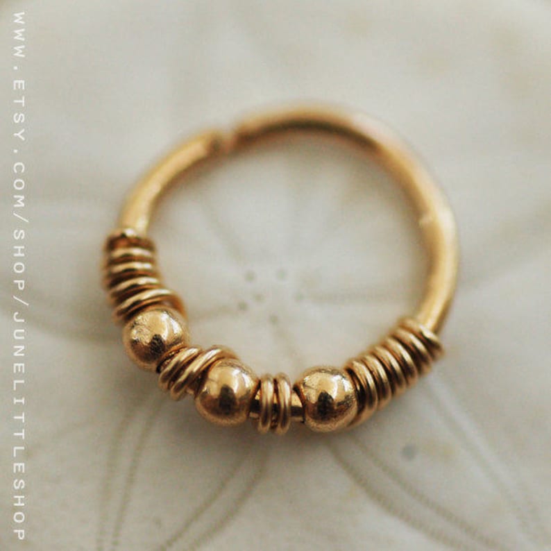 Pu&ograve; includere: Orecchino a cerchio in oro con un design a filo intrecciato e tre piccole perle dorate.