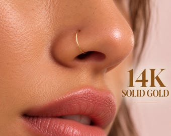 Może przedstawiać: Cienki, okrągły złoty kolczyk do nosa w kształcie koła noszony w skrzydełku nosa. Obraz zawiera tekst 14K SOLID GOLD napisany szeryfową czcionką, wskazujący na skład materiałowy biżuterii widocznej na tym zbliżeniu.