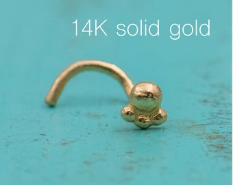 May include: A 14K solid gold nose ring with a small, flower-shaped design. The ring is curved and has a small bead at the end.