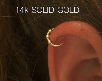 May include: A close-up of a person's ear with a 14k solid gold hoop earring. The earring is made of small, round beads.