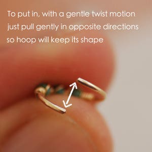 Pu&ograve; includere: Primo piano di un orecchino a cerchio d'oro con una piccola pietra verde. L'anello &egrave; leggermente aperto, mostrando come inserirlo in un piercing. Il testo "To put in, with a gentle twist motion just pull gently in opposite directions so hoop will keep its shape" &egrave; visibile sopra l'anello.