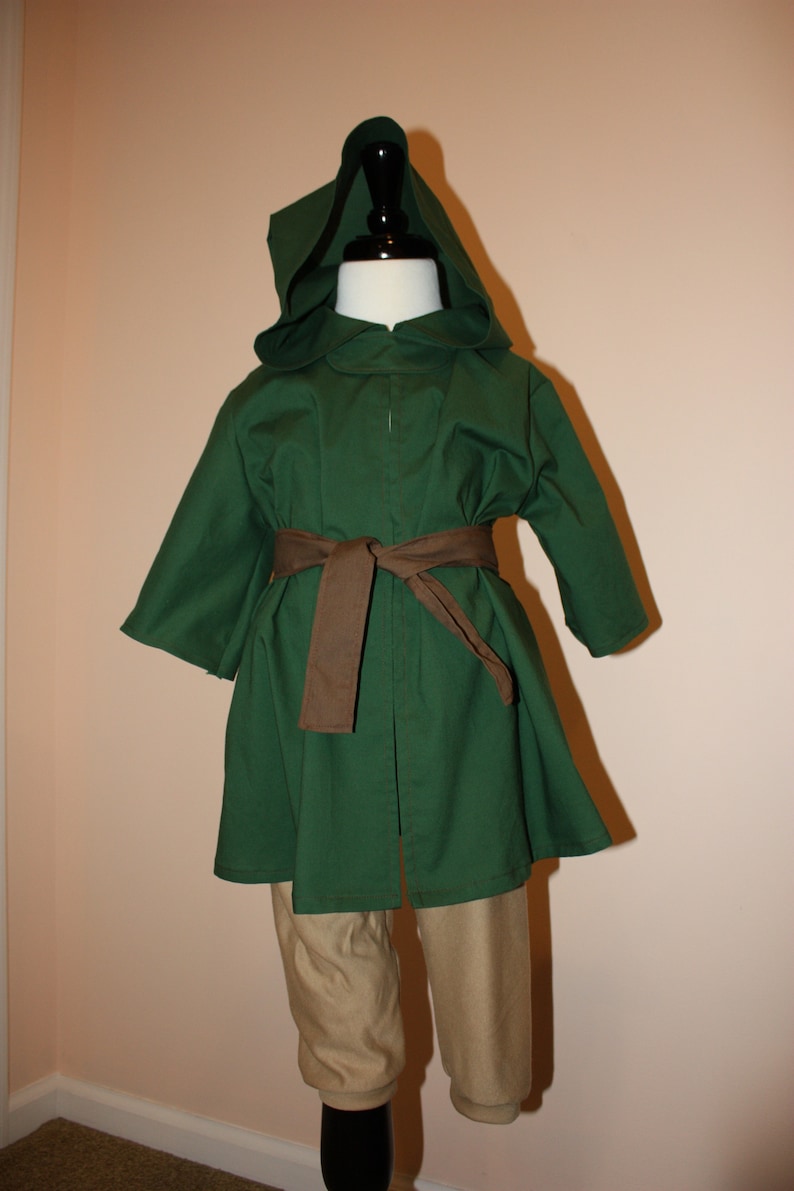 May include: A green hooded robe with a brown belt, worn over tan pants. The robe has a long, flowing design and a pointed hood.