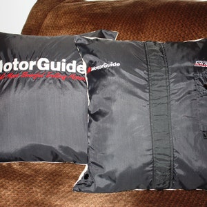 May include: Two black pillows with white piping. One pillow has the text "MotorGuide" embroidered on it in white with the words "World's Most Trusted Trolling Motors" in smaller white text underneath. The other pillow has the text "Stealth" embroidered on it in white.