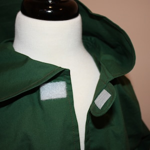 May include: A dark green hooded jacket with a white velcro closure on the front.