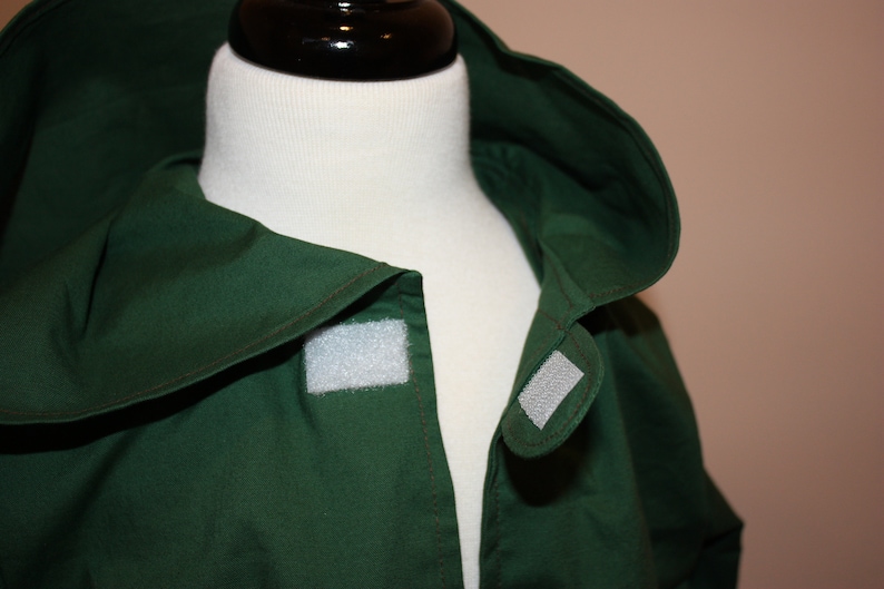 May include: A dark green hooded jacket with a white velcro closure on the front.