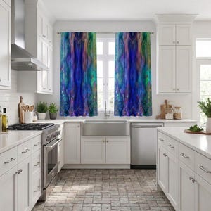 May include: Kitchen with white cabinets, stainless steel appliances, and a stone floor. The focal point is a window adorned with two abstract art curtains in shades of blue, purple, and green, adding a splash of color to the room.