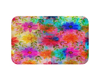May include: A colorful bath mat with a floral pattern. The mat features a variety of flowers in shades of pink, red, yellow, blue, and green. The flowers are arranged in a random pattern on a white background.