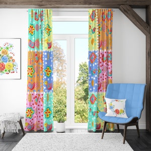 May include: A pair of colourful curtains with a patchwork design featuring birds, flowers, and polka dots. The curtains are hung in a window with a view of trees and a wooden beam.