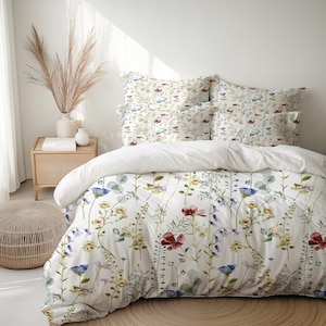 May include: White floral bedding set featuring a duvet cover and pillowcases. The design includes a variety of colorful wildflowers in red, blue, yellow, and purple. The bedding is set on a bed with a white comforter.