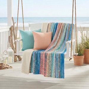 May include: A white porch swing with a colorful striped blanket, two throw pillows, and a cream-colored blanket. The pillows are teal and peach. The blanket has vertical stripes of blue, peach, and cream. The swing hangs from rope.