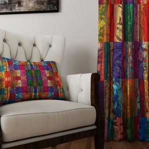 May include: A white armchair with a colorful patterned pillow. The armchair is in front of a colorful patterned curtain.