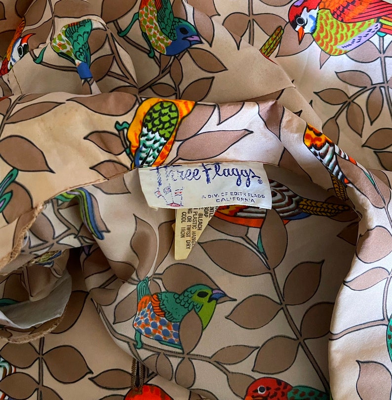 May include: A beige fabric with a repeating pattern of colorful birds and leaves. The fabric has a label that reads "Free Flaggs, A Div. of Edith Flaggs, California".