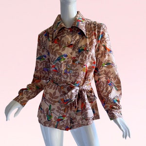 May include: A long-sleeved blouse with a brown background and a colorful bird print. The blouse has a collar and a tie at the waist.