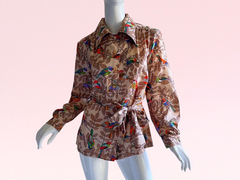 May include: A long-sleeved blouse with a brown background and a colorful bird print. The blouse has a collar and a tie at the waist.