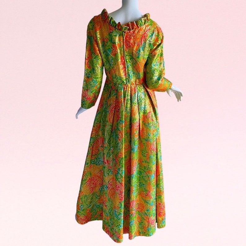 May include: A long-sleeved, green, orange, and pink patterned dress with a ruffled neckline. The dress has a fitted bodice and a full skirt.