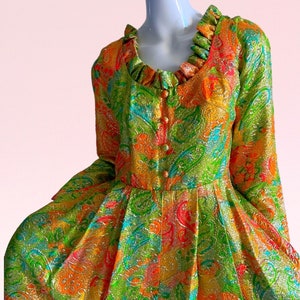 May include: A vintage dress with a green, orange, and pink paisley pattern. The dress has a ruffled neckline and long sleeves.