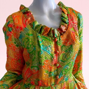 May include: A vintage dress with a colorful paisley pattern in shades of orange, green, gold, and blue. The dress has a ruffled neckline and button closures.