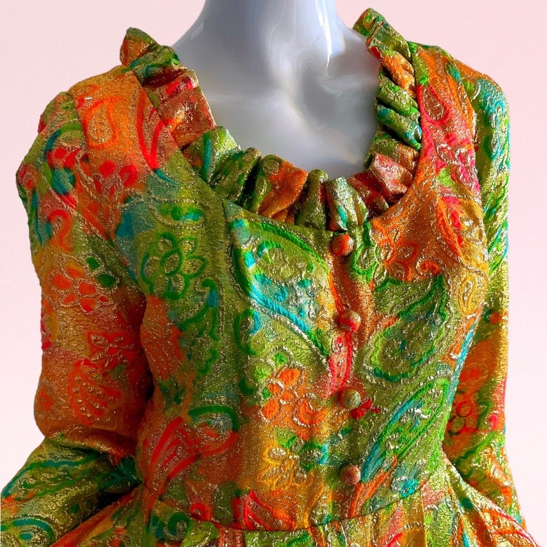 May include: A vintage dress with a colorful paisley pattern in shades of orange, green, gold, and blue. The dress has a ruffled neckline and button closures.