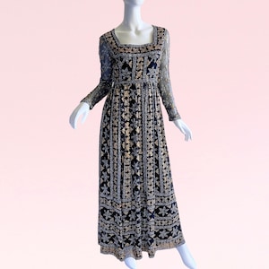 Puede incluir: Un vestido largo de lentejuelas negro y dorado con escote cuadrado y mangas largas. El vestido tiene un corpiño ajustado y una falda fluida.