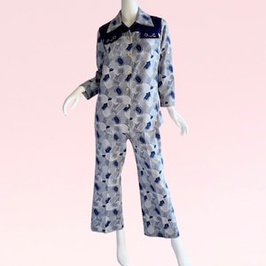 Puede incluir: Un traje de pantalón azul y blanco con estampado con una camisa de cuello y mangas largas. La camisa tiene un cuello y un canesú azul marino con detalles dorados.