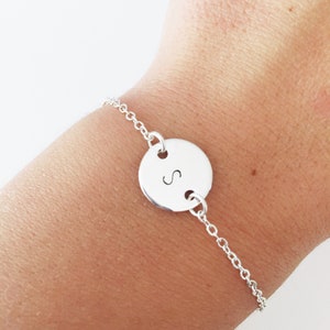 May include: A silver chain bracelet with a round charm featuring the letter "S" engraved on it.