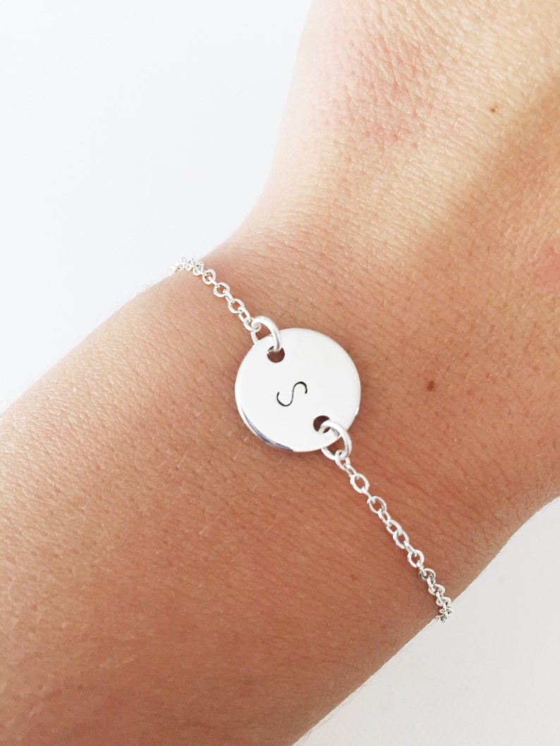 May include: A silver chain bracelet with a round charm featuring the letter "S" engraved on it.
