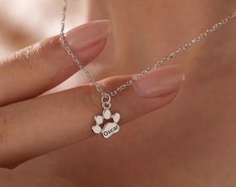 May include: Silver necklace with a paw print charm engraved with the name "Oscar".