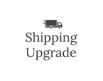 Può includere: Su sfondo bianco, testo "Shipping Upgrade" in carattere serif, sormontato da una silhouette nera di un camion di consegna con linee di movimento.