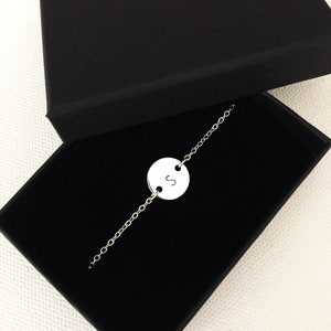 May include: A silver chain bracelet with a round charm featuring the letter "S" in a black box.
