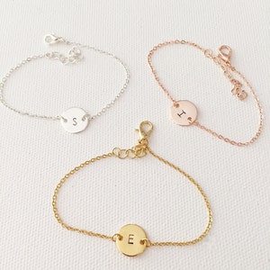 May include: Three delicate chain bracelets with a round charm featuring a single letter. The bracelets are silver, rose gold, and gold, and the charms are engraved with the letters S, I, and E.