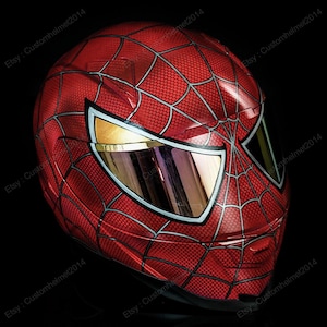 Puede incluir: Un casco de moto rojo y negro con un diseño de Spiderman. El casco tiene una visera transparente y un patrón de telaraña en la parte delantera.