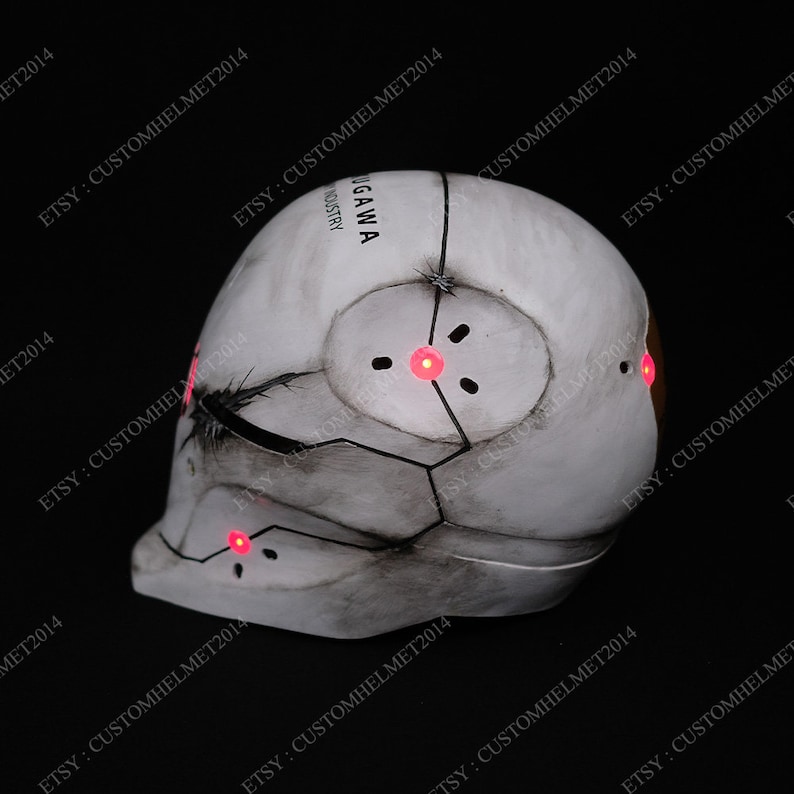 May include: A white helmet with a black and gray design. The helmet has red lights on the side. The text "UGAWAN INDUSTRY" is printed on the helmet.