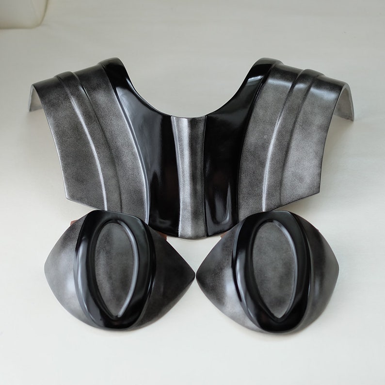 May include: A set of three black and silver plastic costume pieces. The pieces are shaped like a collar and two shoulder pads.