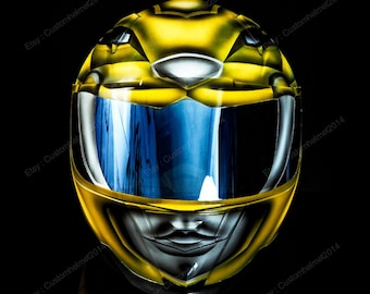 May include: A yellow motorcycle helmet with a blue visor. The helmet is painted with a design that resembles a superhero's face.