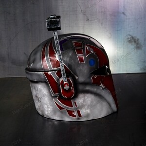 May include: A gray, red, and blue helmet with a weathered, distressed look. The helmet has a raised design on the side and a small, black antenna on top.