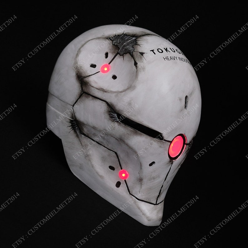 May include: A white helmet with a weathered, distressed look. The helmet has a cracked surface and a black visor. The helmet has red LED lights on the front and top. The text "TOKUGI HEAVY INDUS" is printed on the side of the helmet.