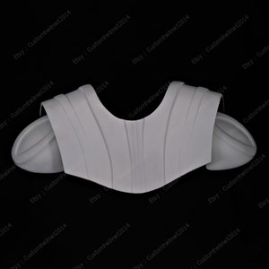 May include: A white plastic molded costume piece for a shoulder armor set. The piece has a textured surface and is designed to fit over the shoulders.